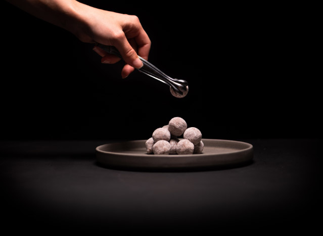 Hand mit Pralinenzange drapiert Tartufi auf grauem Teller auf dunklem Hintergrund