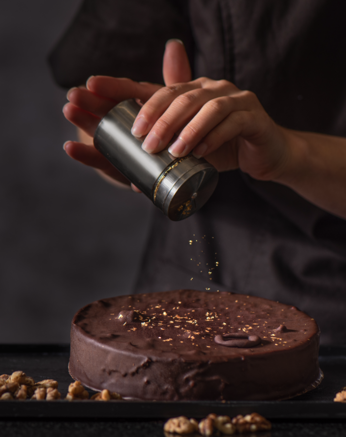 Hände veredeln die Nobile Mutzen Torte mit Goldstreusel auf dunklem Hintergrund