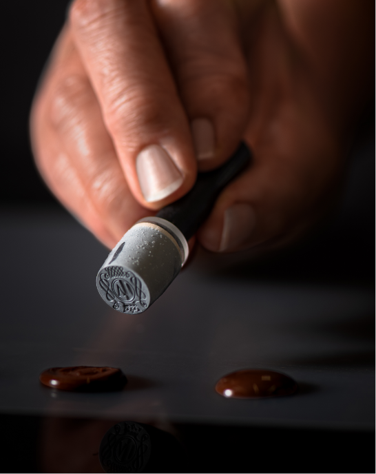 Hand mit Stempel für Siegel aus Schokolade für Casa Nobile Produkte auf dunklem Hintergrund